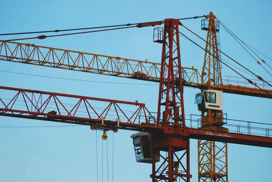 Grues de chantier rouges et orange sous ciel bleu à Paris, site sécurisé par des agents de sécurité et surveillance de chantier